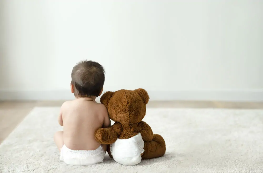 Bébé de dos assis à côté d'un ours en peluche
